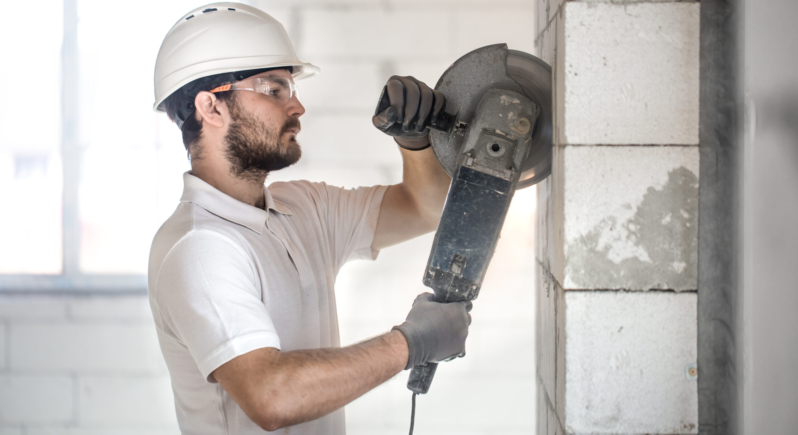 The industrial Builder works with a professional angle grinder to cut bricks and build interior walls. Professional on the construction site. The concept of electrician and handyman. House and reconstruction of the house.